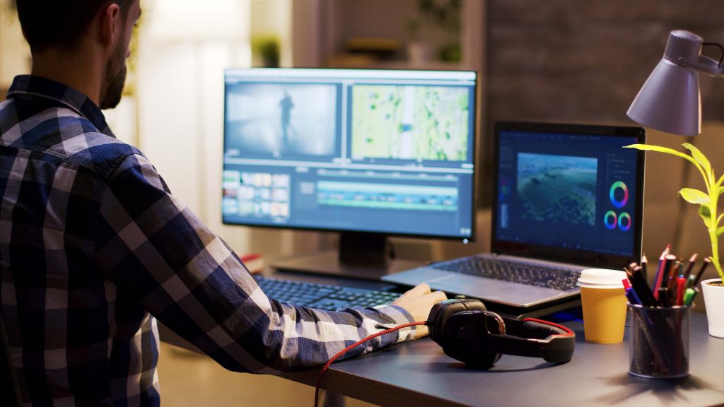Homme assis devant un ordinateur, travaillant dans des logiciels de montage et de retouche.