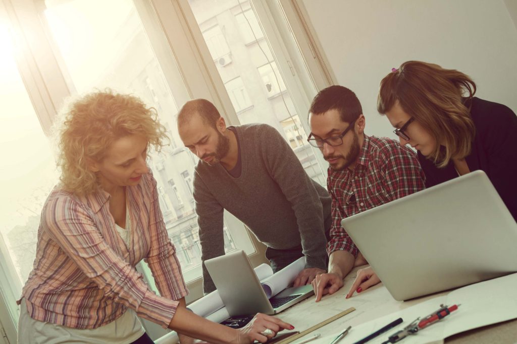 Équipe de quatre personnes installés à une table et regardant des plans architecturaux.