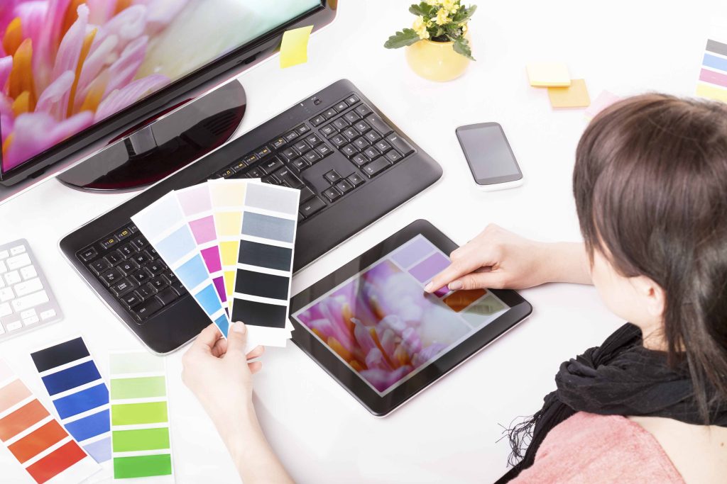 Femme assis devant un ordinateur qui regarde des chartes de couleur ainsi qu'un agencement de couleurs sur une tablette.