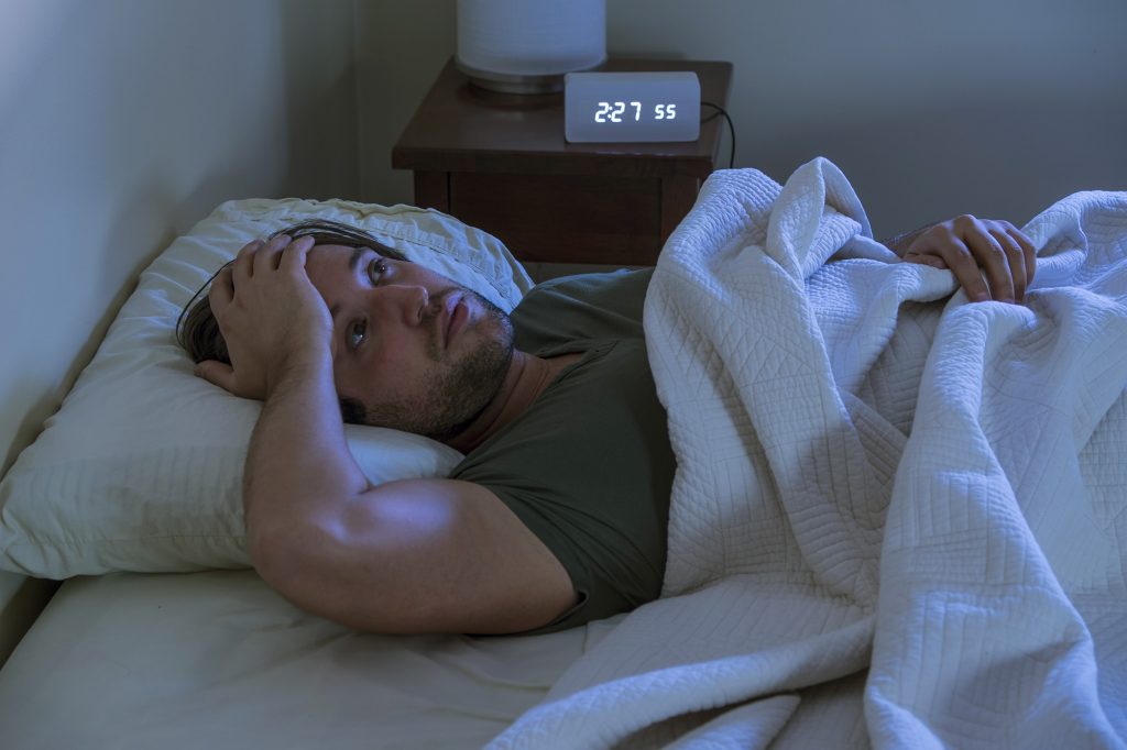 Un homme couché dans son lit, se tenant le front, n'arrivant pas à s'endormir.