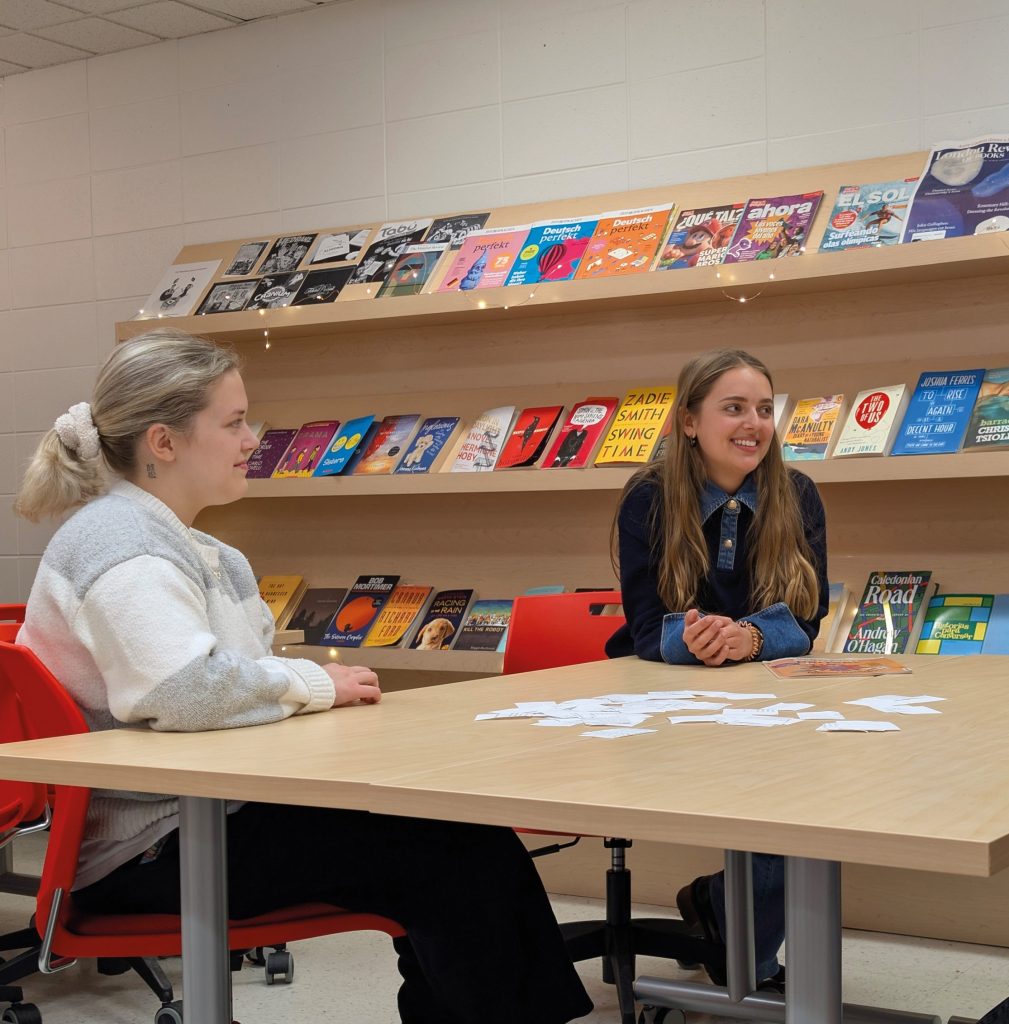Deux étudiantes assises à la table dans un Centre de langues, devant un bibliothèque remplies de livres