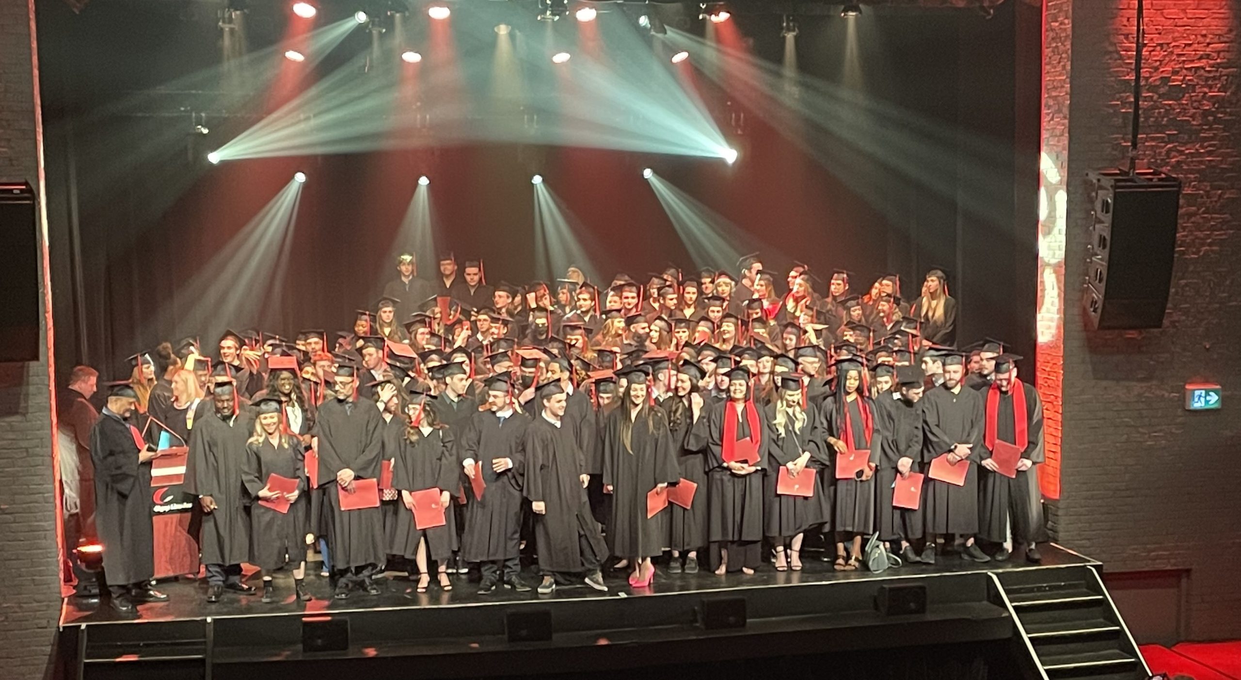 Groupe de finissants et de finissantes en toge sur scène lors de la collation des grades.