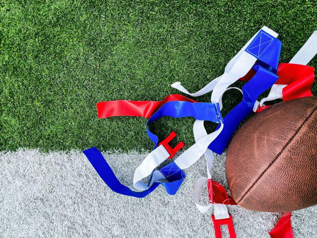 un ballon de football déposé sur un terrain gazonné, avec des lanières de tissu de couleurs rouge, bleue et blanche à côté.