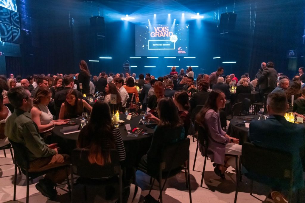 Une foule de personnes assises autour des tables rondes dans la salle Montaigne, devant la scène