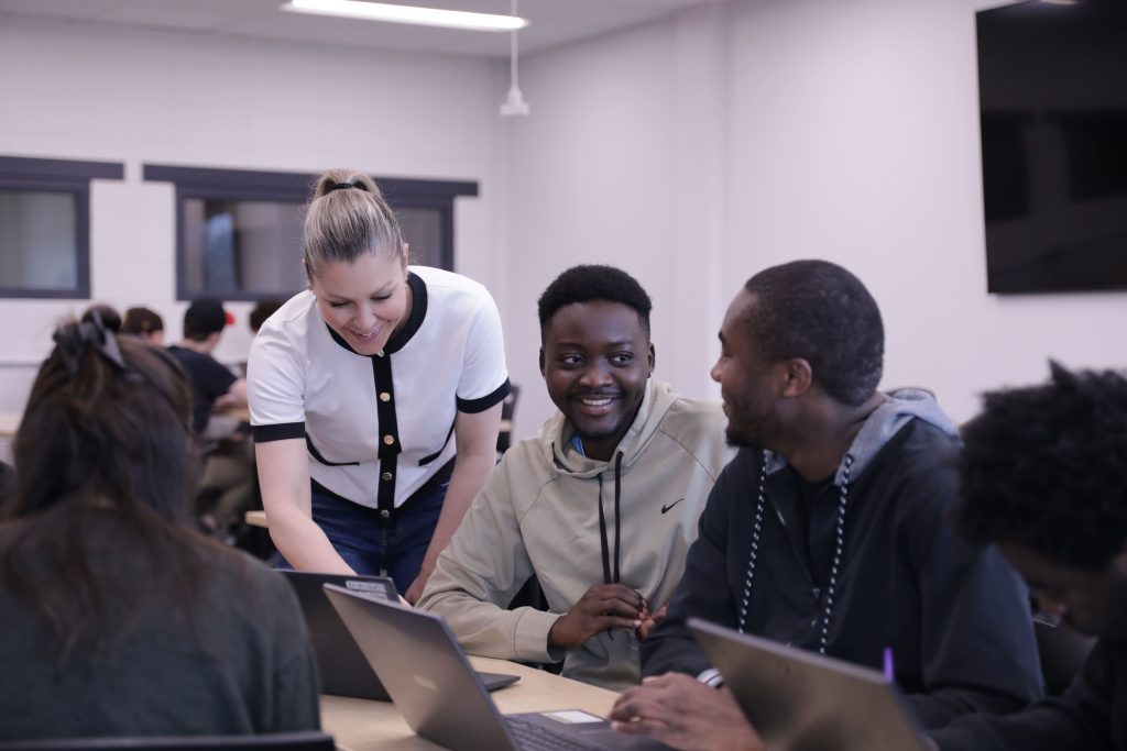 Des étudiants souriants qui sont en travail d'équipe et sont assis autour d'une table avec leurs ordinateurs portables.
