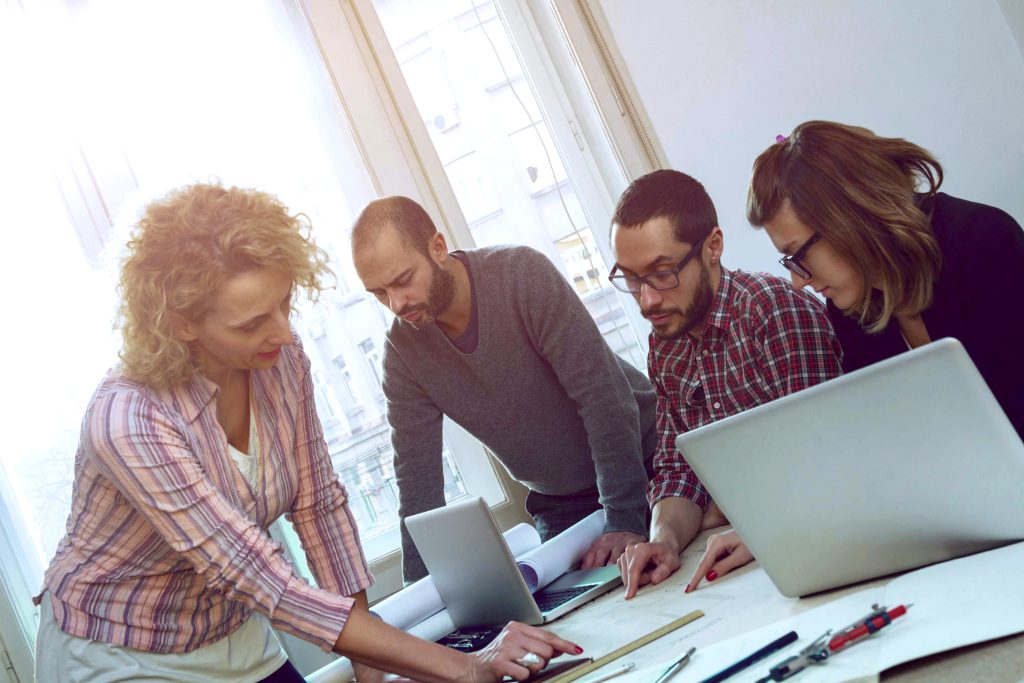 Équipe de quatre personnes installés à une table et regardant des plans architecturaux.