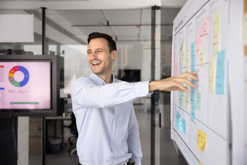 Homme souriant qui montre du doigt une information sur une affiche blanche avec des post-it colorés