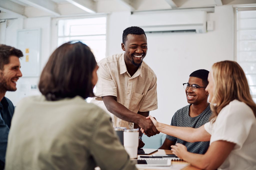 Groupe cinq individus, dont un homme souriant qui serre la main à une femme