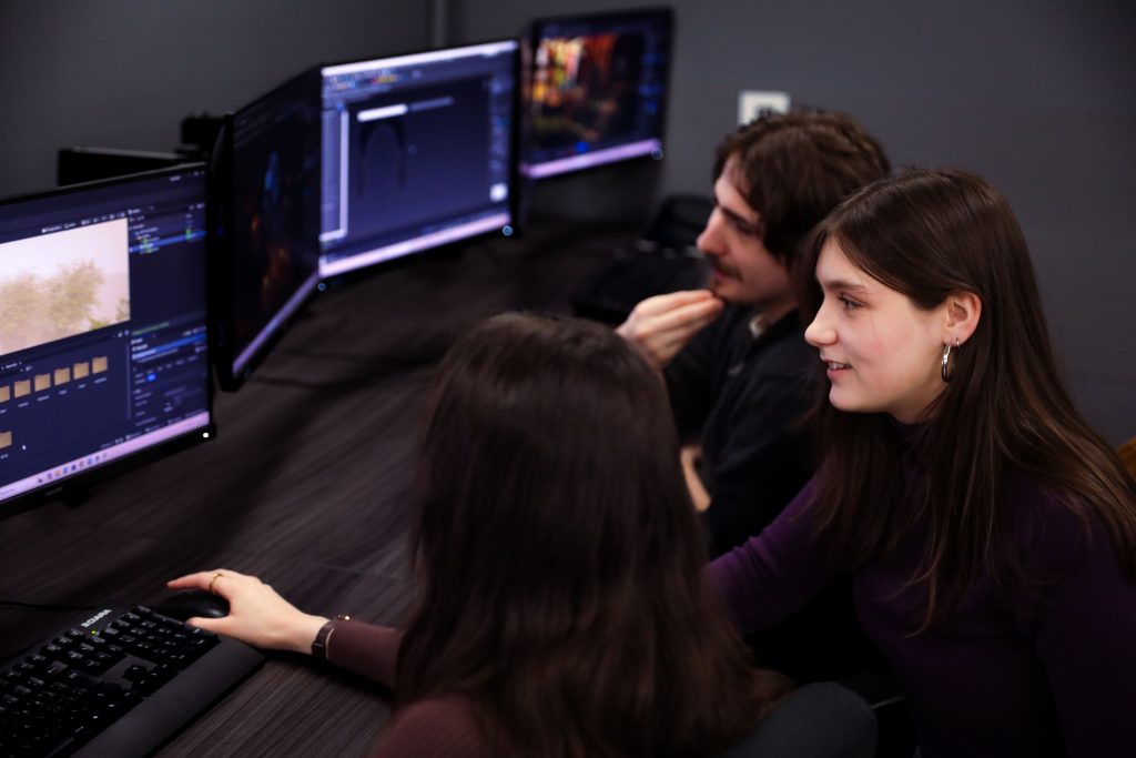 Trois étudiants travaillent sur un projet d'animation 3D face à plusieurs écrans d'ordinateur.