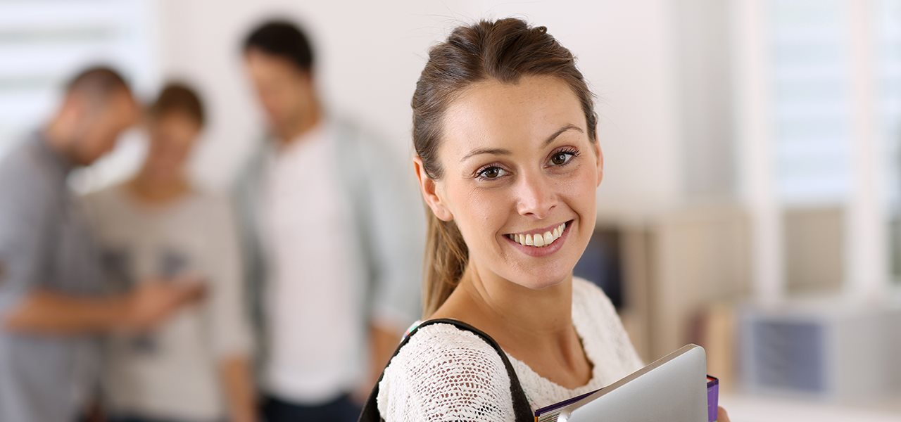 Étudiante souriante tenant son portable en première plan, trois étudiants flous à l'arrière