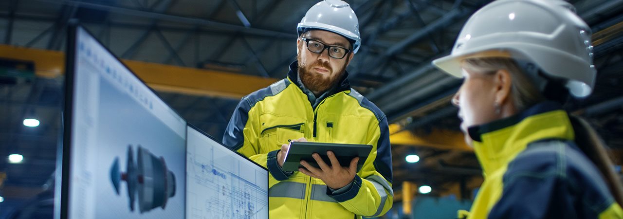 Femme vérifiant des données sur un ordinateur et homme vérifiant des données sur une tablette électronique dans une usine