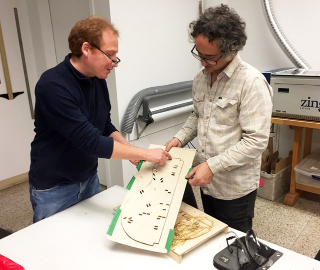 Enseignants en lutherie en train d’analyser la découpe au laser d’un gabarit de table d’harmonie d’une petite guitare. 