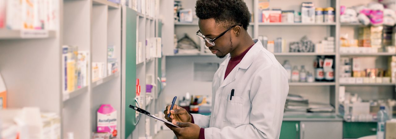 Jeune homme devant des étagères remplies de médicaments d'une pharmacie