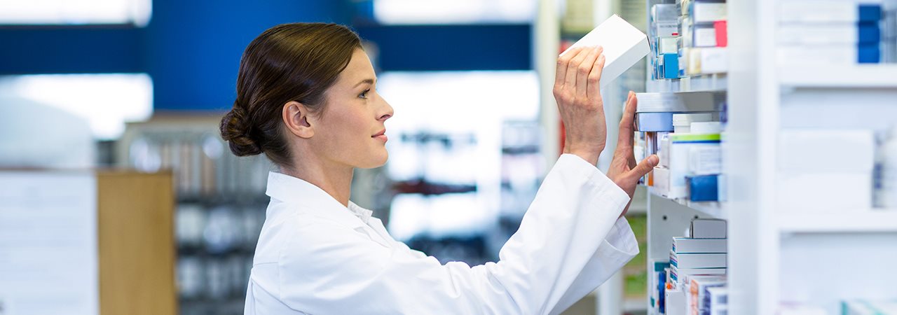 Technicienne en pharmacie qui place une boite sur une étagère de médicaments