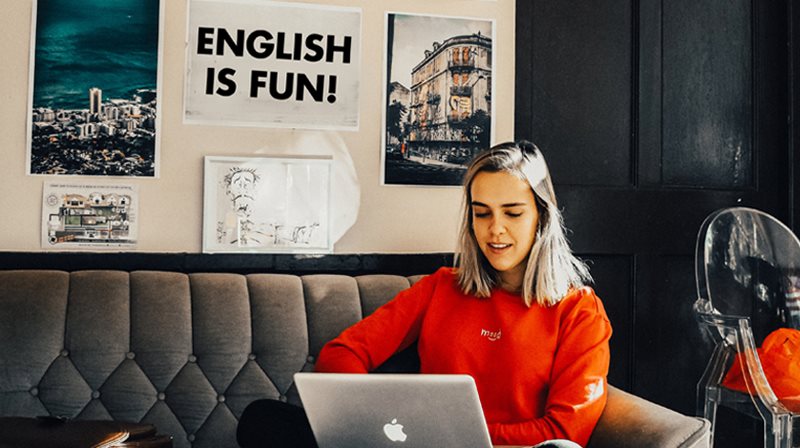 jeune fille qui travaille sur un ordinateur portable, arrière-plan affiches au mur : ville, édifice, English is fun