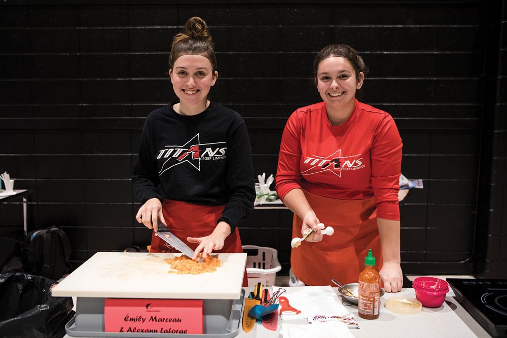 Deux étudiantes souriantes à leur station lors du concours Moi je cuisine!