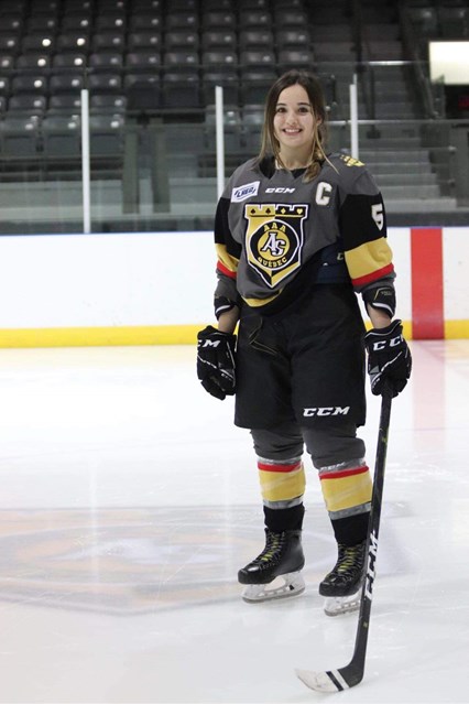 Emmie Carbonneau, souriante en uniforme sur la glace avec son bâton de hockey