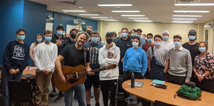 Thomas Hellman tenant sa guitare dans une salle de classe accompagné d'étudiants de Sciences humaines