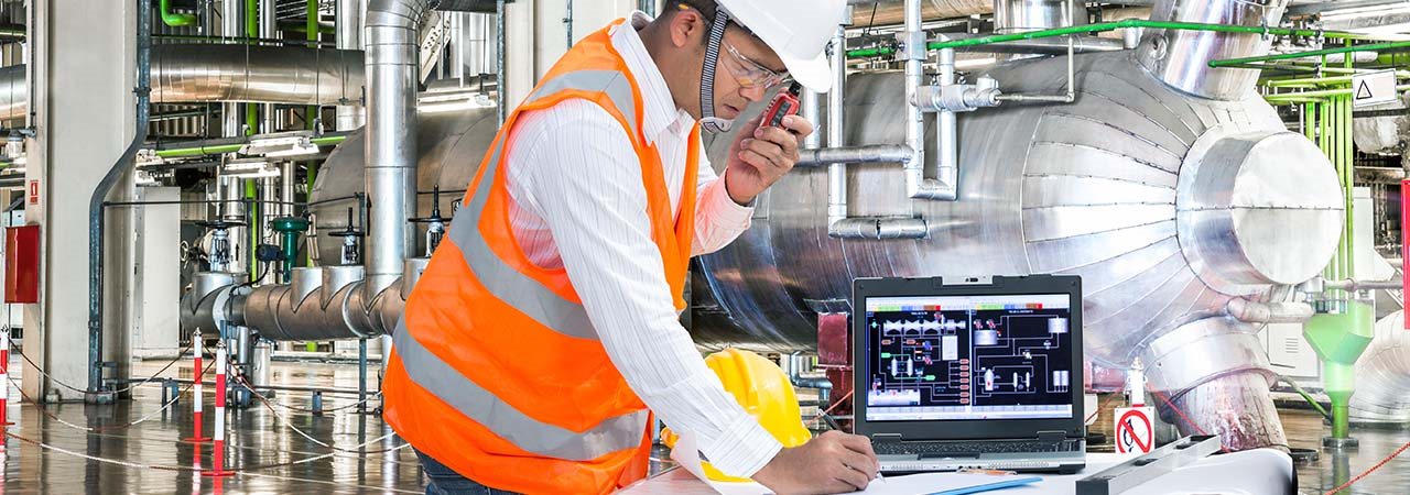 Travailleur dans une usine parlant sur un walkie-talkie avec dossard et casque de construction qui écrit sur un plan