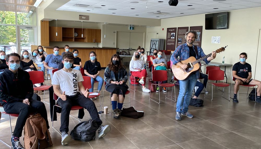 Thomas Hellman tenant sa guitare accompagné d'étudiants de Sciences humaines