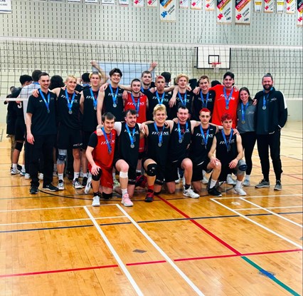 Joueurs de volleyball masculin division 2 au centre du terrain devant le filet, souriants avec leurs médailles au cou