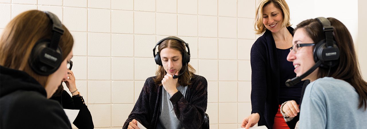 Étudiants, casque d'écoute sur les oreilles, et leur enseignante autour d'une table