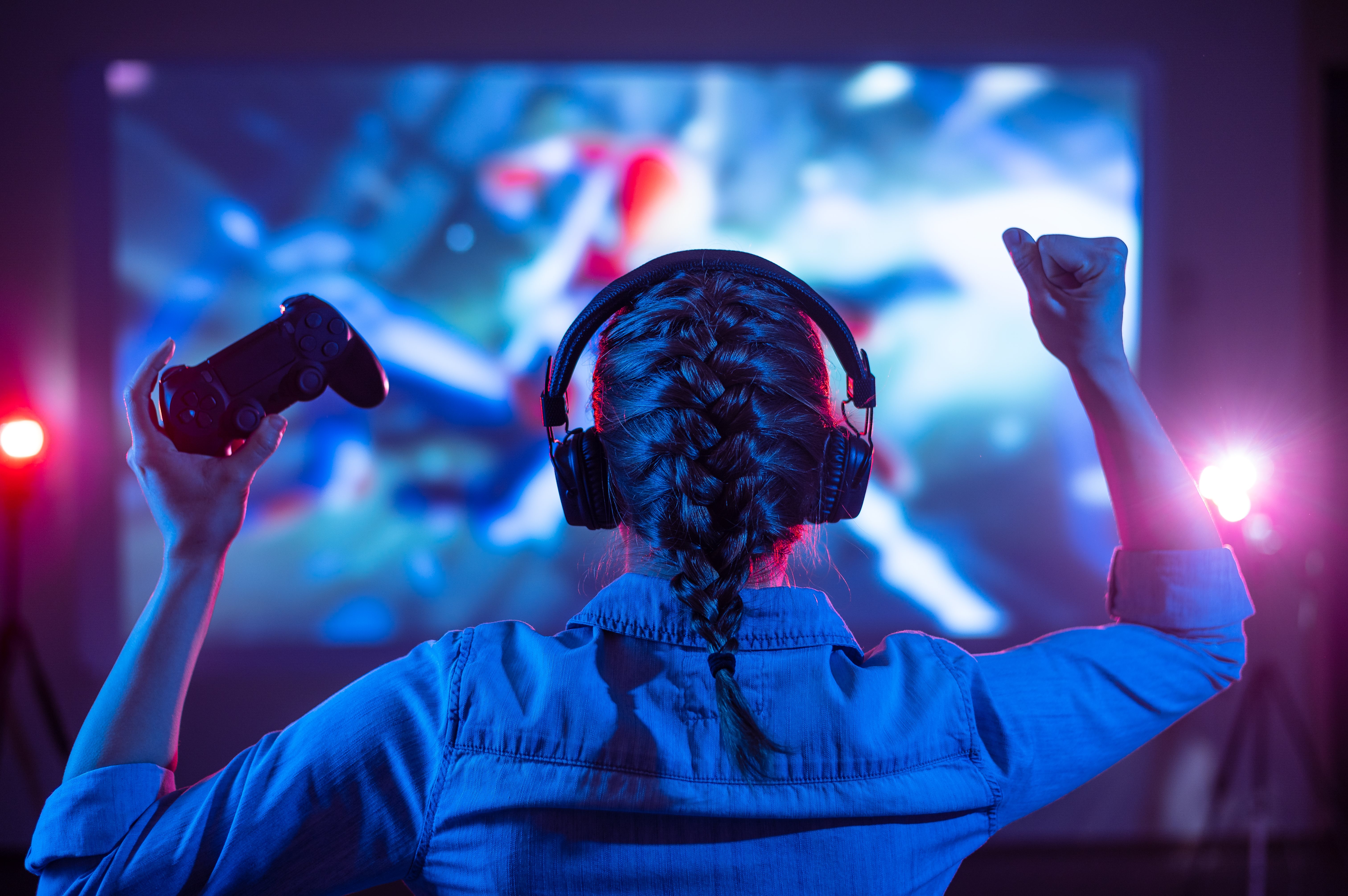 Une joueuse de jeu vidéo, manette à la main et poing dans les airs, devant un écran