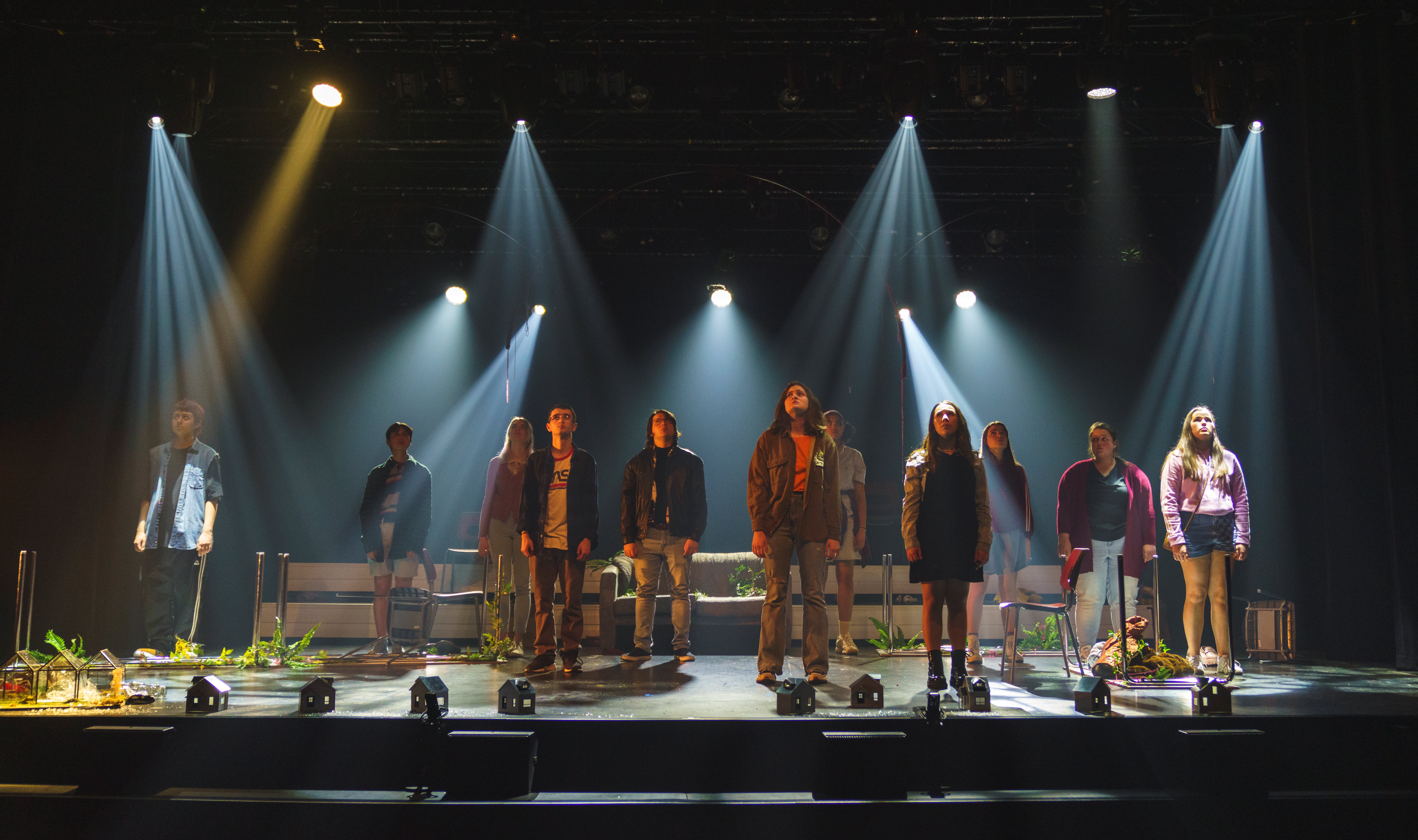 Une dizaine d'étudiants de la troupe de théâtre du Grand escalier, debout sur scène entourés de maisons minuscules