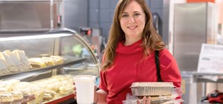 Une femme tient plusieurs plats emballés devant le comptoir de la cafétéria