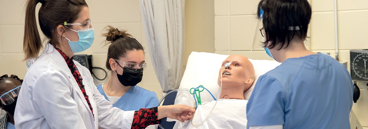 Futures étudiantes en soins infirmiers portant le masque de procédure qui examinent un mannequin dans un laboratoire simulant une chambre d'hopital 