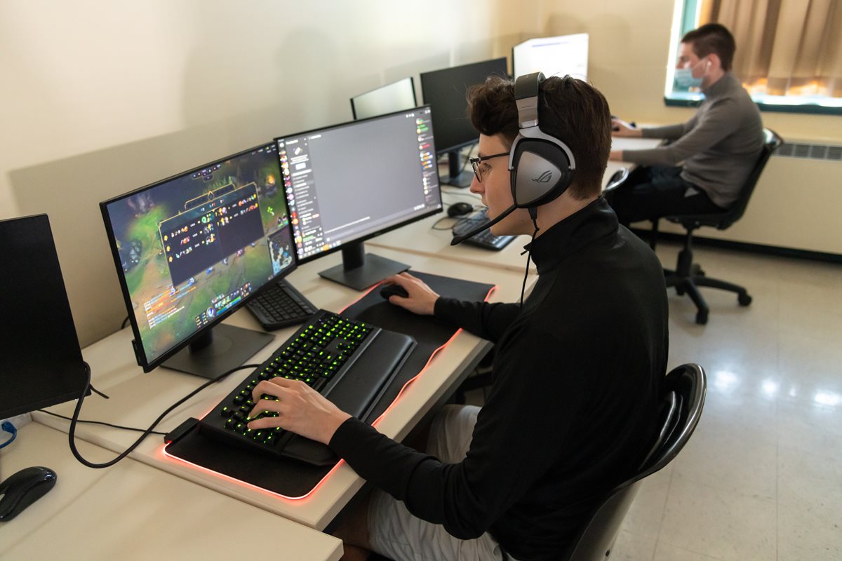 Jeune homme avec écouteurs devant deux écrans d'ordinateur en compétition de sport électronique