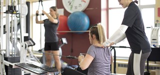 Une femme utilise un appareil de musculation sous le regard attentif de son entraîneur