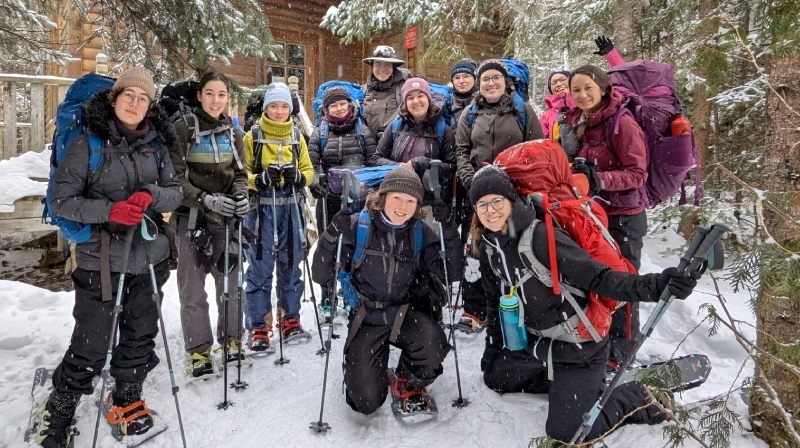 Le groupe sourient à la caméra en forêt sous une légère tombée de neige.