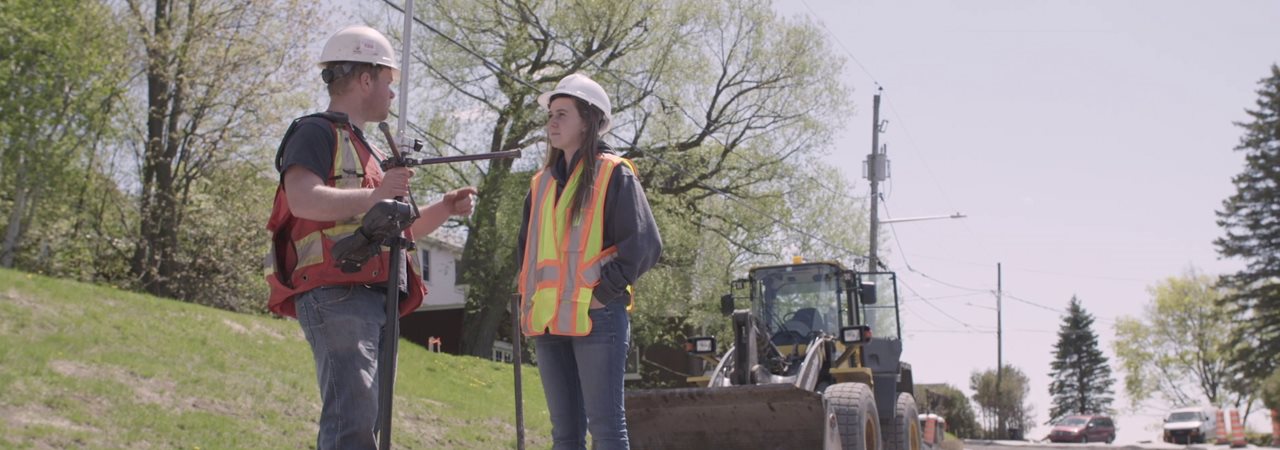 Étudiants en génie civil sur un chantier avec casque et veste de sécurité, machinerie lourde à l'arrière