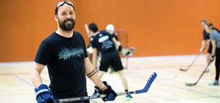 Un homme tenant un bâton de hockey souriant devant un match de hockey cosom