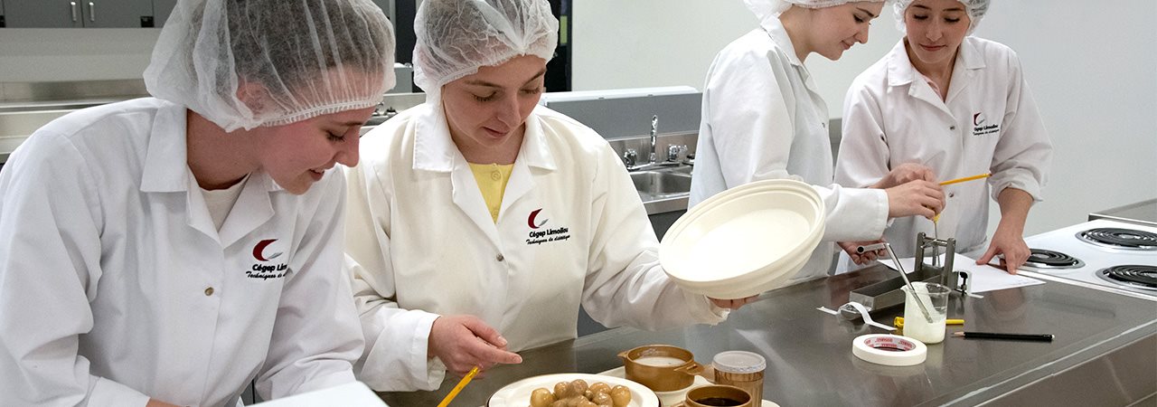 Étudiantes souriantes, en uniforme, devant une assiette de nourriture dans un laboratoire de diététique